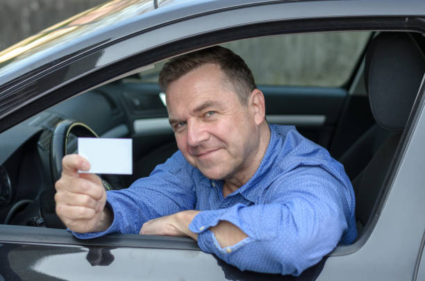 istock Middle aged man leaning from a car showing his licence 658054874