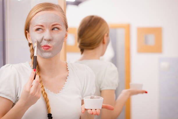 istock Happy young woman applying mud mask on face 658064630