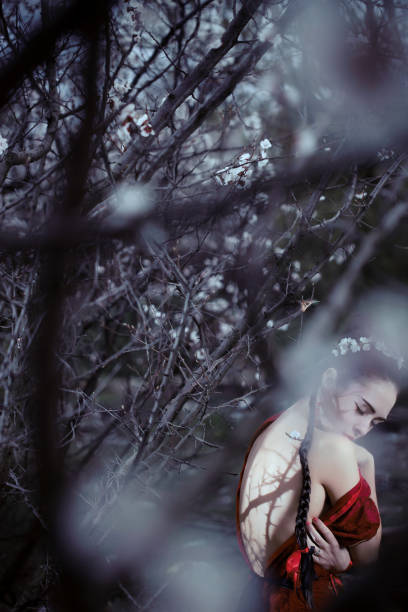 Sad asian woman in kimono alone in blossoming garden. Female with naked back and shadows from tree branches like scars on it. Creative photo outdoor on the nature.