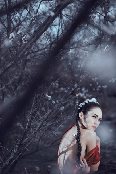 Sad asian woman in kimono alone in blossoming garden. Female with naked back and shadows from tree branches like scars on it. Creative photo outdoor on the nature.