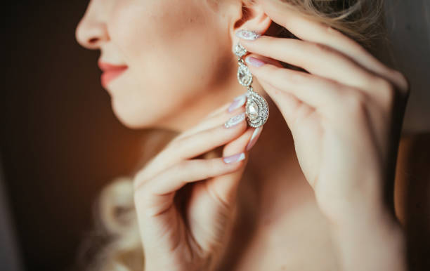 Wedding preparation. Beautiful, happy bride dresses earrings before wedding. Wedding accessories, jewelry. Closeup portrait of bride. Selective focus.