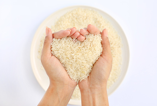 Hand holding Jasmine white rice in shape of love on white plate against white background