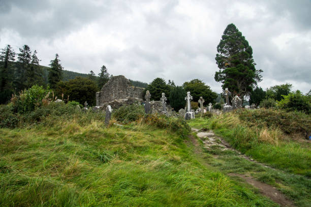 Old ruins of buildings, headstones, and Celtic crosses in an abandoned cemetery in Glendalough, Ireland. Cloudy day in the cemetery.