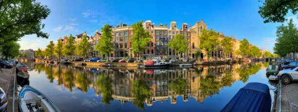 Beautiful 180 degree panoramic panorama of the UNESCO world heritage Keizersgracht canal  in Amsterdam, the Netherlands, on a sunny summer day with a blue sky and mirror reflection