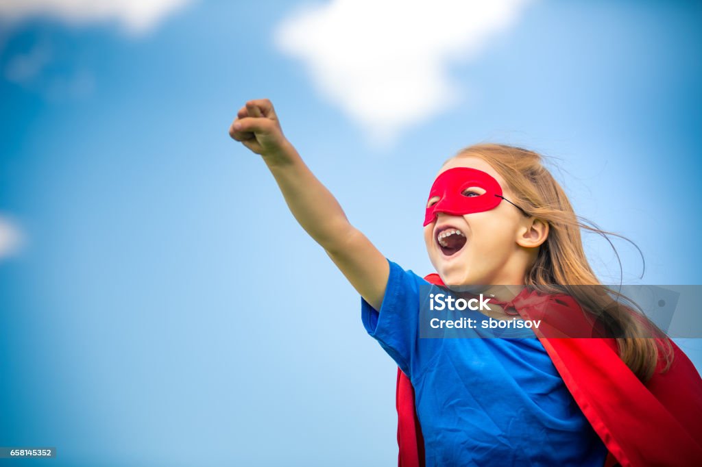 Funny little girl playing power super hero. Funny little girl playing power super hero over blue sky background. Superhero concept. Child Stock Photo