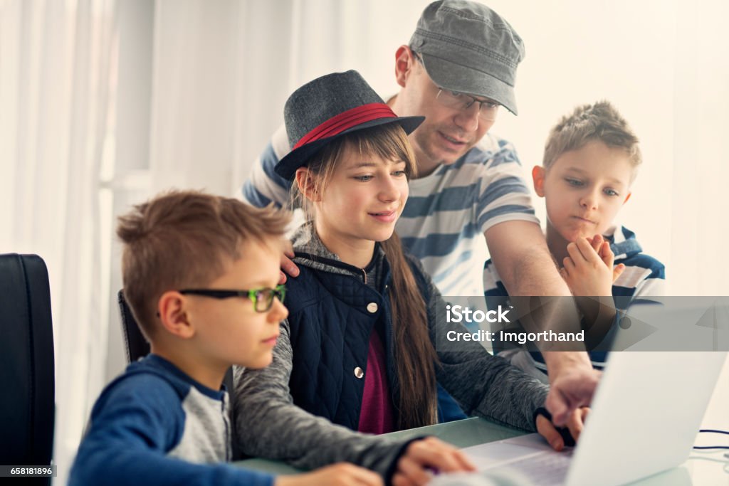 Father helping kids with coding their homework Father is helping kids in computer science project. The girl aged 11 is using modern ultrabook laptop. Sunny day.
 Happiness Stock Photo