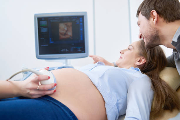 Loving couple attending doctor for pregnancy ultra sound procedu Beautiful mature pregnant couple smiling looking at the sonogram results on ultrasound scanner monitor while on a checkup at the gynecologist pregnancy love family parents maternity doctor clinic. medical scanner photos stock pictures, royalty-free photos & images