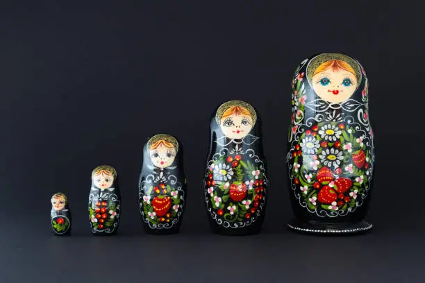 Beautiful black russian nesting dolls (matryoshka) dolls with white, green and red painting in front of dark background