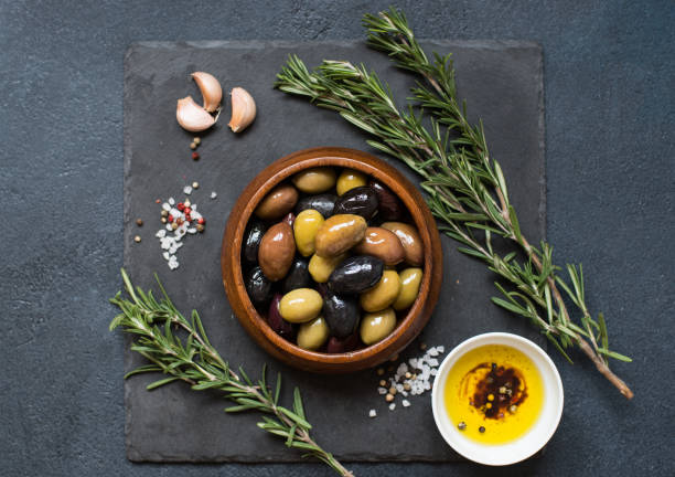 Olives, rosemary and olive oil Olives and olive oil on dark stone background. Green, red and black olives in a wooden bowl, top view green olive fruit stock pictures, royalty-free photos & images