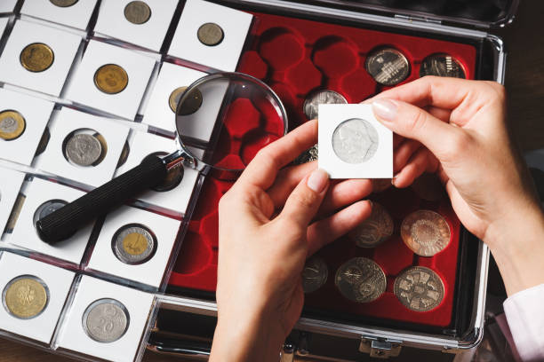 Box with collectible coins and magnifying glass Box with collectible coins in the cells and a page with coins in the pockets, soft focus background coin collection stock pictures, royalty-free photos & images