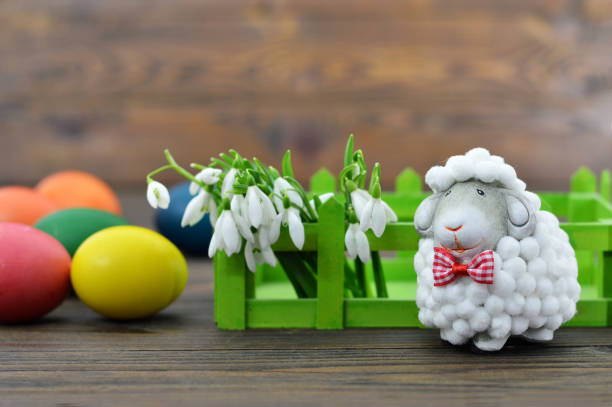 Easter eggs, spring flowers and cute sheep figurine on wooden background
