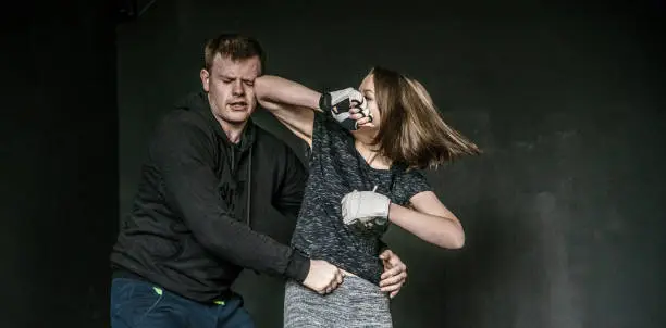 Strong gritty modern women practicing the self-defense martial art Krav Maga, used in the Israel Army. The trainee in the sporting club in Minsk, Belarus. Woman self-defense trick against the man's attack.