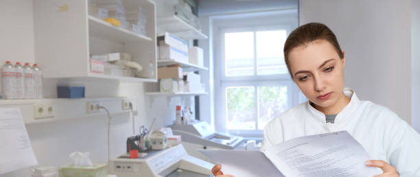 istock Young female scientist reading printed notes in scientific laboratory, panoramic image 658318060
