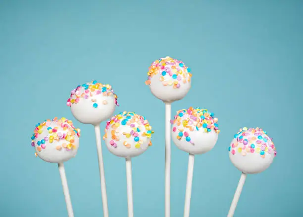 Vanilla cake pops with colorful sprinkles over a blue background.