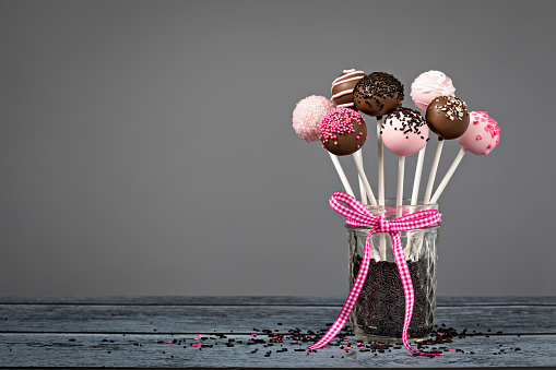 Assortment of chocolate cake pops in a jar with a cute pink bow over a grey background.