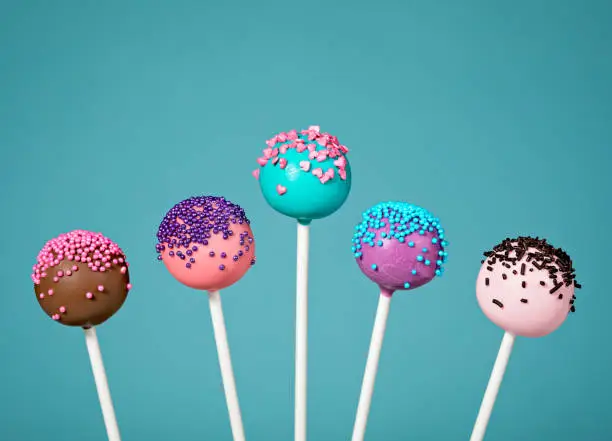 Colorful cake pops with sprinkles over a teal blue background.