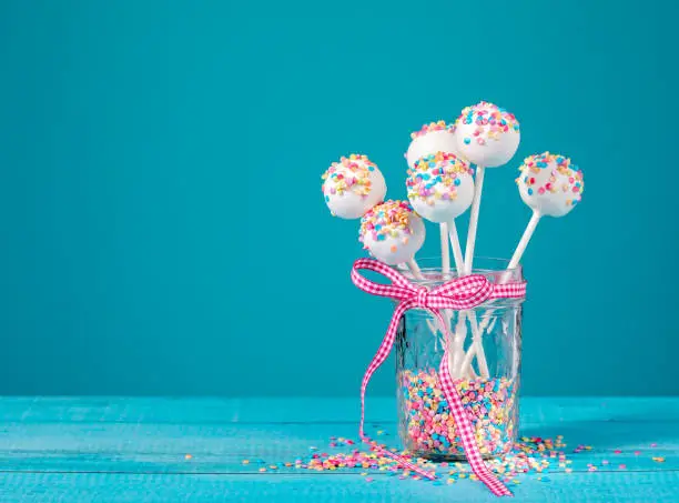 Vanilla cake pops with colorful sprinkles in a cute jar over a blue background.