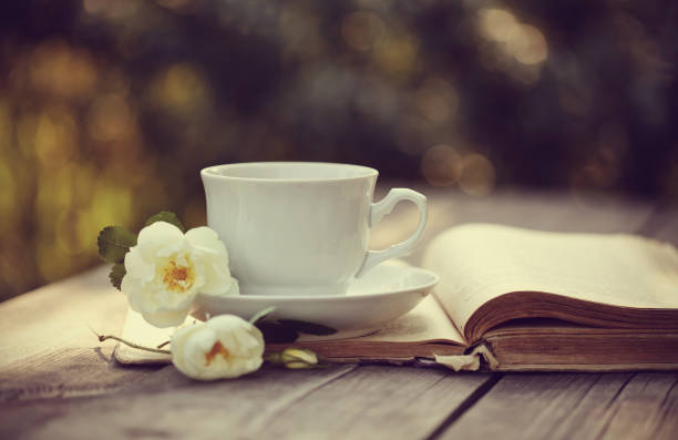 istock White cup with a flowers of wild rose on an open old book 658324818