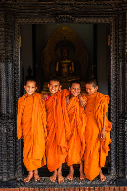 Novice Buddhist monks looking out of the doors in the monastery in Bhaktapur, Nepal. Bhaktapur is an ancient Newar town in the east corner of the Kathmandu Valley, Nepal. It is the third largest city in Kathmandu valley and was once the capital of Nepal during the great Malla Kingdom until the second half of the 15th century. Bhaktapur is listed as a World Heritage by UNESCO for its rich culture, temples, and wood, metal and stone artwork.