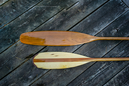 Single-bladed canoe paddles on a wood dock. The wood on the dock is arranged in an angular pattern.