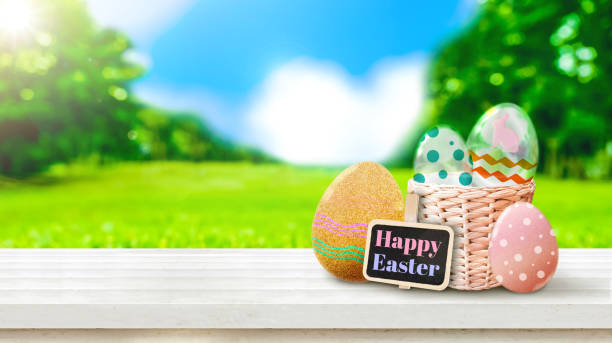 istock Happy easter word on clip board and easter eggs and bunny icon on white plank wood tabletop with green field with blur park background. 658348300