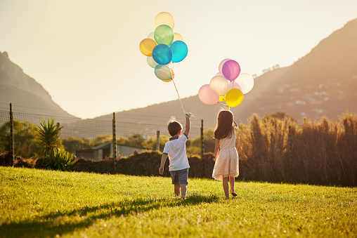 Rearview shot of two cute little siblings holding balloons while walking outside