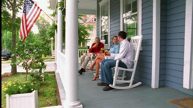 A young couple talks with a retiree on his front porch.