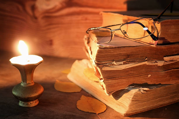istock old tattered book on a wooden table lighted candle and glasses 658381254