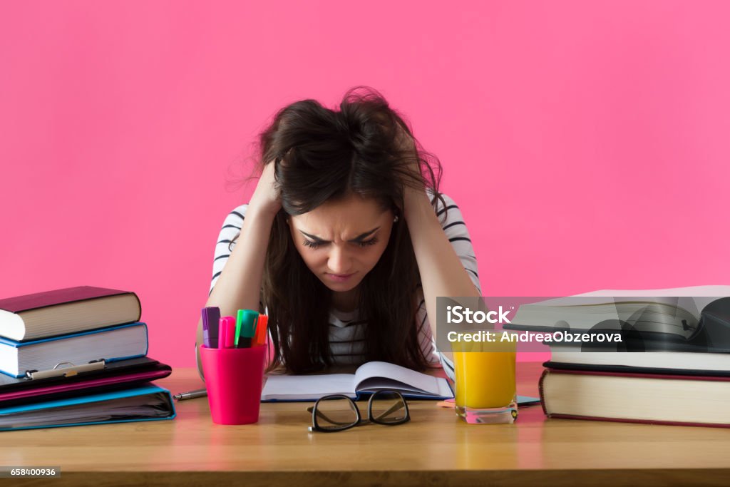 Young student with desperate expression sitting at her desk. Frustrated female student. Young student with desperate expression sitting at her desk. Emotional Stress Stock Photo