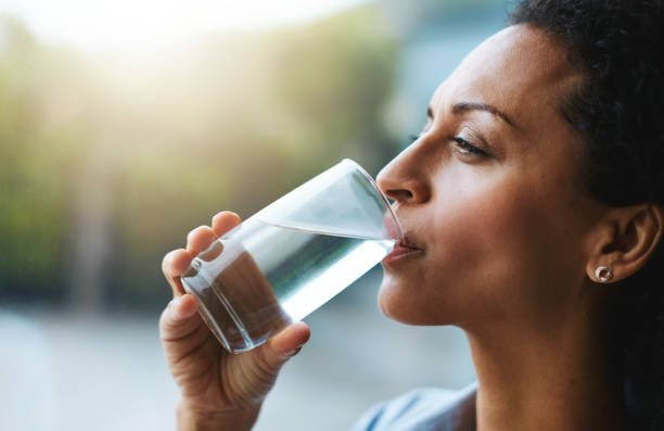 Hydration is her beauty secret Shot of a woman drinking a glass of water at home glass of water stock pictures, royalty-free photos & images