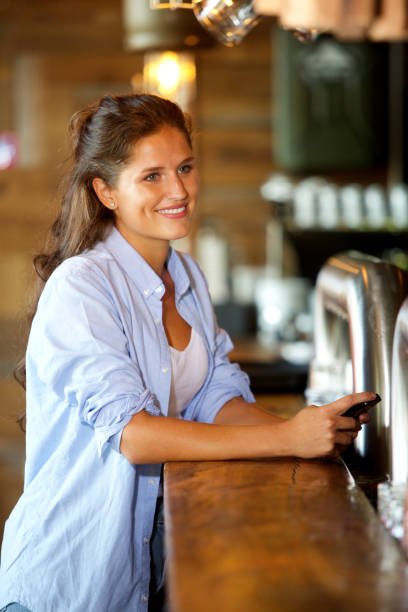 istock smiling woman standing at the bar using mobile 658431034