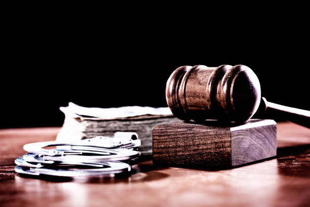 Judge's gavel with banknotes and handcuffs on courtroom desk A wooden judge's gavel with a stack of banknotes, possibly symbolising  bribery and problems in the justice system, plus a pair of handcuffs, symbolising crime. criminal justice stock pictures, royalty-free photos & images