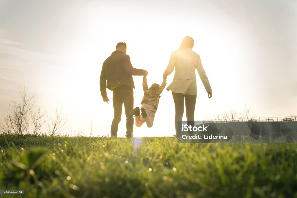 Happy family heaving fun in the park. Happy parents playing with their daughter in the park. Space for copy. From behind. Family Stock Photo