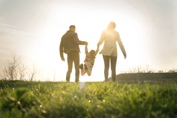 Happy family heaving fun in the park. Happy parents playing with their daughter in the park. Space for copy. From behind. three men holding hands stock pictures, royalty-free photos & images