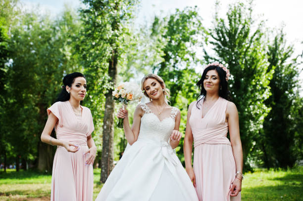 istock Bride posed on park with two cute brunette bridesmaids on pink dresses. 658447054