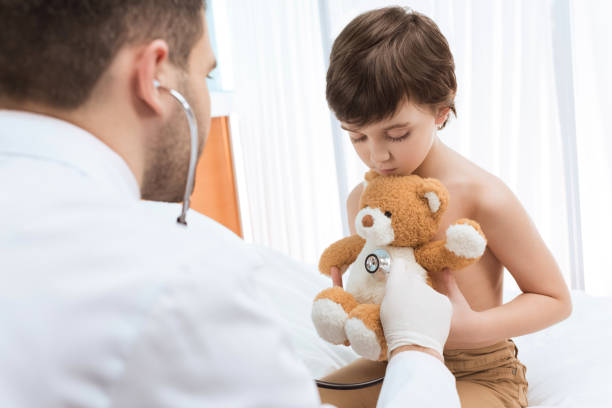 istock Man doctor with stethoscope examining little boy holding teddy bear 658447434
