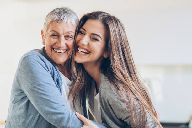 Happy adult mother and daughter embracing Senior and young women embracing at home arm around photos stock pictures, royalty-free photos & images