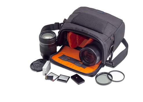 Open shoulder camera bag, two different photo lenses and some photo accessories on a light background