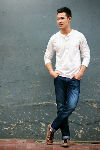 Shot of a handsome young man standing with his hands in his pockets against a grey wall