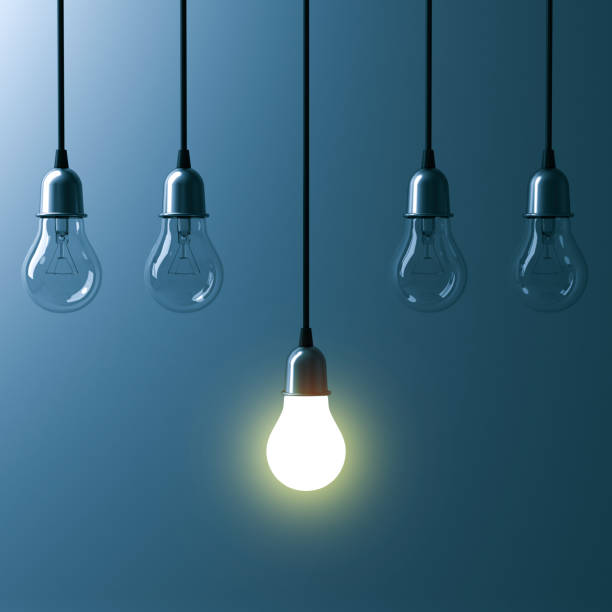 istock One hanging light bulb glowing different and standing out from unlit incandescent bulbs with reflection on dark cyan background , leadership and different business creative idea concept. 3D render 658483586