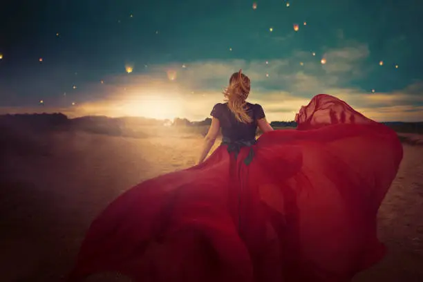 rear view of young woman with red dress flying in the wind, enjoying freedom, nature and the beauty of sunset.