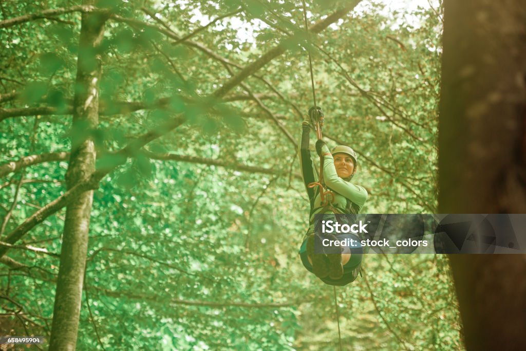 fun time on tyrolean traverse woman with protective equipment enjoying adventure on ride with the tyrolean traverse.photo taken in the forest. Woodland Stock Photo