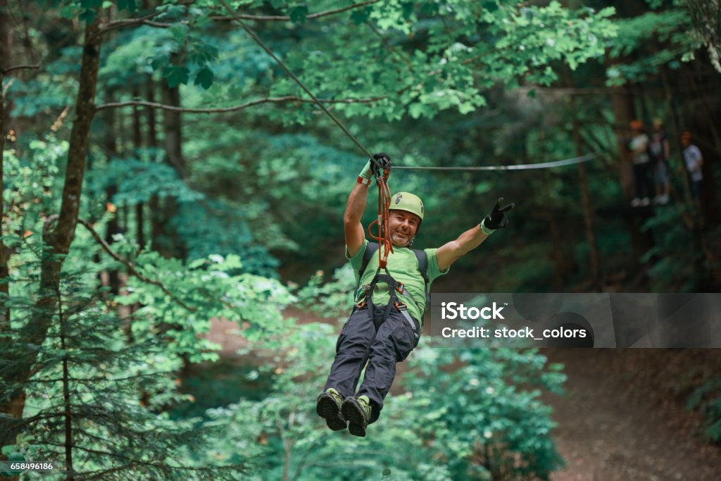 freedom and fun time on tyrolean traverse man enjoying summer day on tyrolean traverse, feeling active and having fun.photo taken in the forest. Tyrolean Traverse Stock Photo