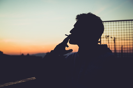 Sunset silhoette of a man smoking on the tof of the building