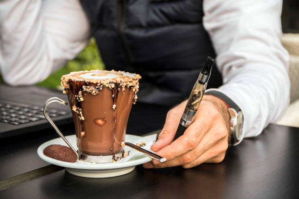 istock man holding vape or electronic cigarette and drinking coffee 658502864
