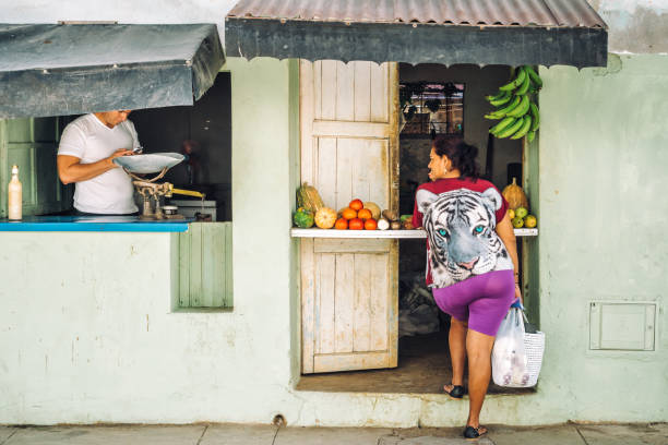 Gibara, Holguin Province, Cuba - February 13, 2017: A small shop in Gibara, also know as 'White town' is one of the most interesting destinations in Holguin province in Cuba. A lady waits at the hatch of a colourful corner shop.