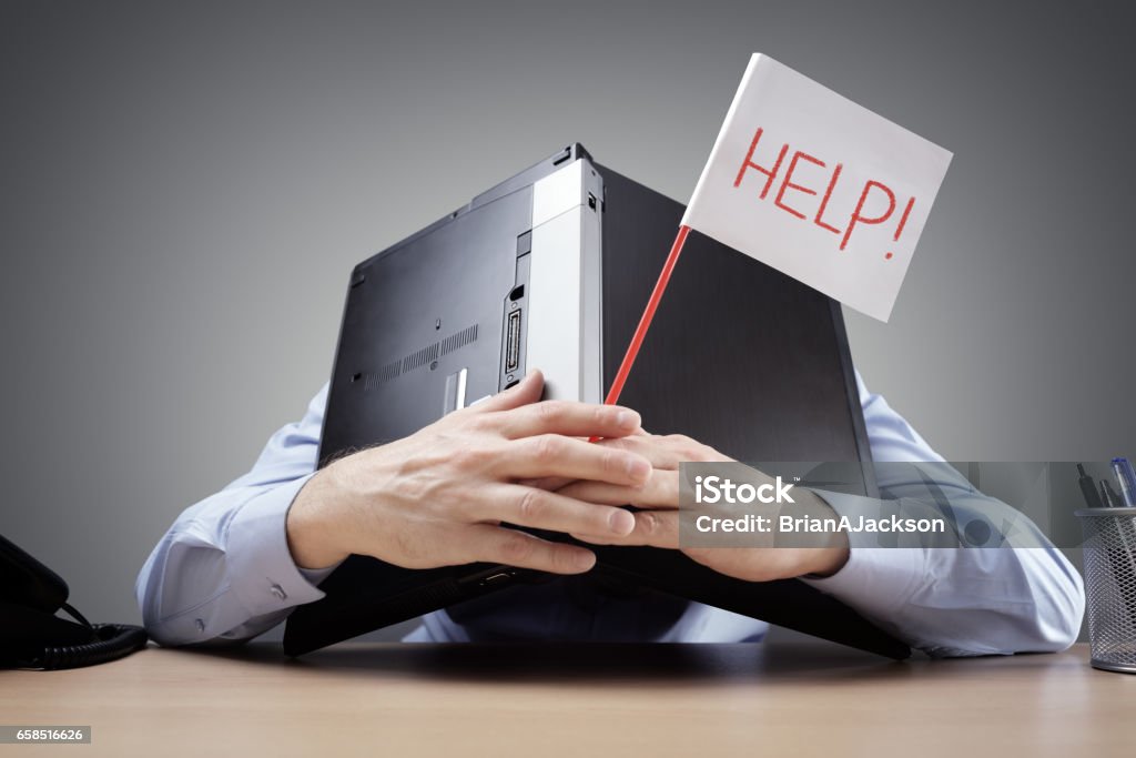 Businessman burying his head uner a laptop asking for help Frustrated and overworked businessman burying his head uner a laptop computer asking for help Frustration Stock Photo