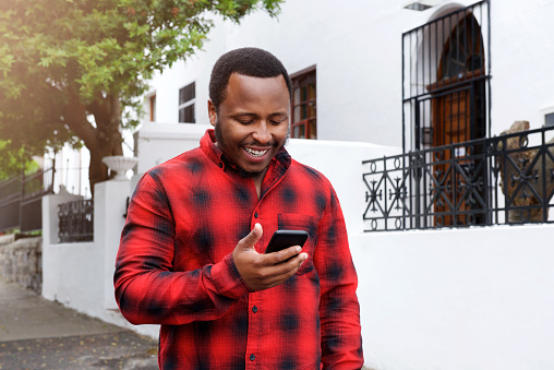 Portrait of a cool black guy smiling outside with cell phone