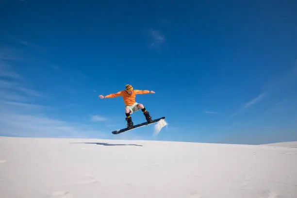 Snowboarder is flying over the sand dune. Snowboarding training in summer season. Sand boarding in desert.