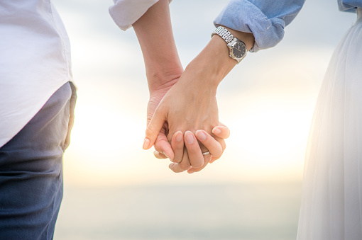 Wedding by lake, man and woman together on deck in nature and love. Beautiful couple relax by the water in the natural afternoon sun, white dress of bride and black wedding suit contrast in sunshine